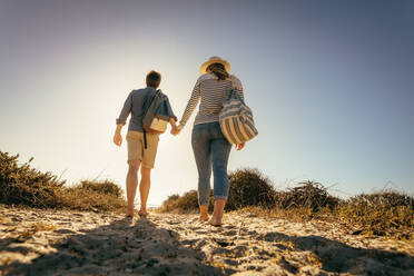 Paar im Urlaub, das zusammen auf dem Sand spazieren geht und die Hand hält. Frau mit Hut geht mit ihrem Freund an einem sonnigen Tag am Strand spazieren. - JLPSF16802