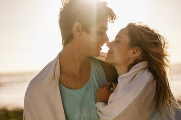 Nahaufnahme eines glücklichen Paares in romantischer Stimmung, das dicht am Strand steht. Ein Mann umarmt seine Freundin im Freien am Meeresufer mit Sonnenschein im Hintergrund. - JLPSF16812