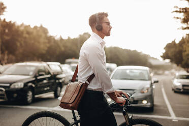 Mann, der mit seinem Fahrrad die Straße auf dem Zebrastreifen überquert. Mann, der die Straße überquert, während er auf dem Weg ins Büro mit drahtlosen Kopfhörern Musik hört. - JLPSF16826