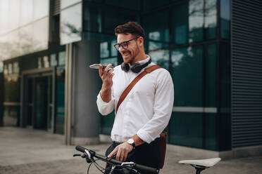 Ein Mann, der mit seinem Fahrrad auf der Straße steht und mit dem Handy über einen Lautsprecher spricht. Ein Geschäftsmann, der mit seinem Fahrrad auf der Straße steht und mit dem Handy spricht. - JLPSF16828