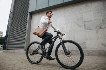 Seitenansicht eines Unternehmers, der mit dem Fahrrad ins Büro fährt. Ein Mann mit Bürotasche fährt mit dem Fahrrad auf der Straße ins Büro. - JLPSF16833