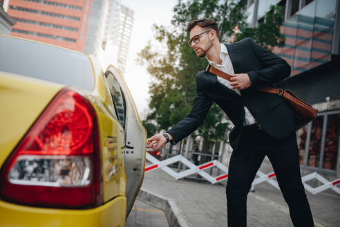 Ein Unternehmer öffnet die Tür eines Taxis, das auf dem Bürgersteig steht. Ein Mann nimmt ein Taxi, um ins Büro zu fahren. - JLPSF16838