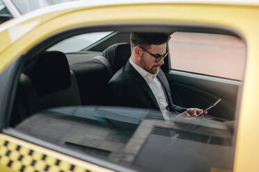 Geschäftsmann, der auf dem Rücksitz eines Taxis sitzt und sein Handy überprüft. Geschäftsmann, der in einem Taxi ins Büro fährt. - JLPSF16840