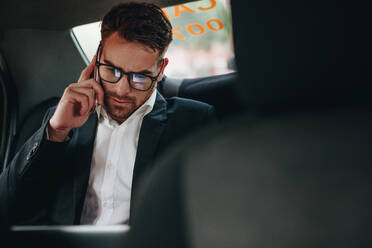 Geschäftsmann bei der Büroarbeit, während er in einem Taxi ins Büro fährt. Unternehmer, der unterwegs im Auto sitzend geschäftliche Aufgaben erledigt. - JLPSF16841