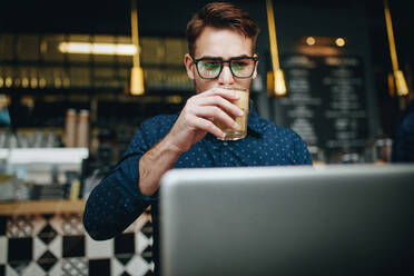 Geschäftsmann, der an einem Laptop arbeitet und Kaffee trinkt, in einem Restaurant sitzend. Unternehmer, der in einem Café sitzend seine Arbeit erledigt. - JLPSF16843