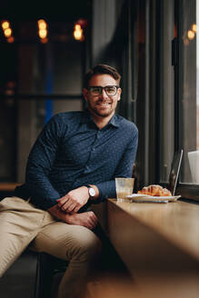 Glücklicher Freiberufler sitzt in einem Restaurant und arbeitet am Laptop. Geschäftsmann sitzt entspannt in einem Restaurant mit Laptop und Essen auf dem Tisch. - JLPSF16853