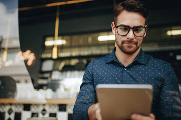 Unternehmer, der in einem Restaurant auf einen Tablet-Computer schaut. Geschäftsmann, der in einem Restaurant sitzt und sein Geschäft leitet. - JLPSF16856