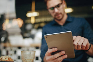 Geschäftsmann, der an seinem Tablet-Computer in einem Restaurant mit Essen auf dem Tisch arbeitet. Freiberufler, der in einem Café mit Essen sitzt und seine Arbeit an einem Tablet-Computer erledigt. - JLPSF16857