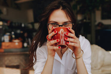 Nahaufnahme einer jungen Frau, die in einem Café Kaffee trinkt. Frau mit Brille trinkt eine Tasse Kaffee. - JLPSF16879