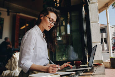 Geschäftsfrau in einem Café, die an einem Laptop arbeitet und sich Notizen macht. Geschäftsfrau, die in einem Café arbeitet. - JLPSF16881