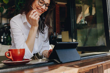 Geschäftsfrau, die in einem Café arbeitet und einen Videoanruf mit einem digitalen Tablet tätigt. Freiberuflerin in einem Café, die einen Videoanruf tätigt. - JLPSF16885