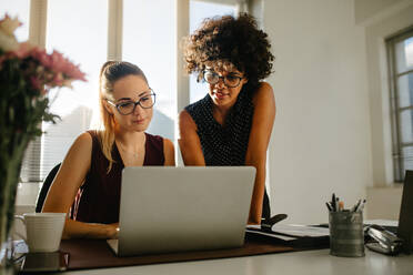 Porträt von zwei Geschäftsfrauen, die auf einen Laptop schauen und ein neues Projekt im Büro besprechen. Junge Geschäftskollegen besprechen die Arbeit im Büro. - JLPSF16911