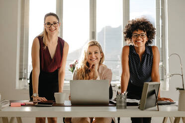 Porträt einer lächelnden jungen Geschäftsfrau, die am Schreibtisch steht und in die Kamera lächelt. Multirassische Geschäftsfrauen im Büro. - JLPSF16915