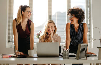 Lächelnde junge Frauen am Arbeitstisch im Büro. Gruppe von drei verschiedenen Frauen im Büro, die lächeln. - JLPSF16916