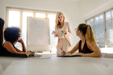 Weibliche Führungskraft, die während einer Vorstandssitzung mit Kollegen über Budget und Einkommen diskutiert. Gruppe von Geschäftsfrauen, die über Finanzen diskutieren. - JLPSF16925