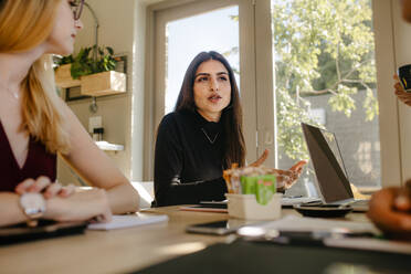 Multiethnische Geschäftsfrauen besprechen einen Plan in einer Sitzung. Eine Frau teilt ihre Ideen mit Kollegen während einer Sitzung in einem Startup-Büro. - JLPSF16932
