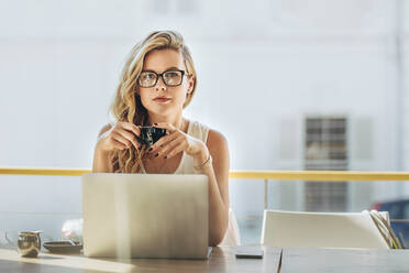 Porträt einer attraktiven jungen Frau, die in einem Café mit Laptop sitzt und Kaffee trinkt. Junge kaukasische Geschäftsfrau, die in einem Coffeeshop Kaffee trinkt. - JLPSF16940