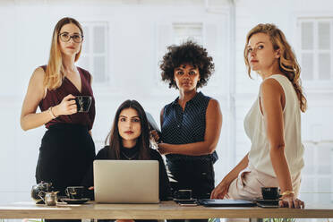 Gruppe von multiethnischen Geschäftsfrauen in Freizeitkleidung, die zusammen an einem Bürotisch sitzen und in die Kamera schauen. Weibliches Startup-Team-Portrait. - JLPSF16942