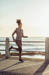 Fit young woman jogging on seaside promenade. Side view of female runner out on a run at sunset. - JLPSF16948