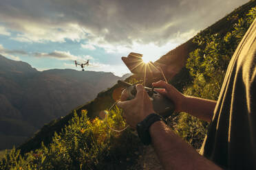 Nahaufnahme eines Mannes, der eine Drohne steuert, die mit einer Fernbedienung über die Berge fliegt. Naturfotograf, der eine Drohne bedient und Bilder von einem Naturschutzgebiet an einem sonnigen Tag macht. - JLPSF16960