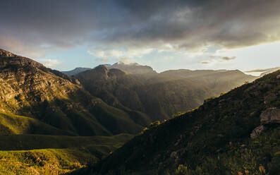 Sonnenstrahlen beleuchten das Bergtal mit dunkler Wolkenlandschaft. Schöne Berge und bewölkter Himmel Sonnenuntergang in Jonkershoek Naturreservat. - JLPSF16964