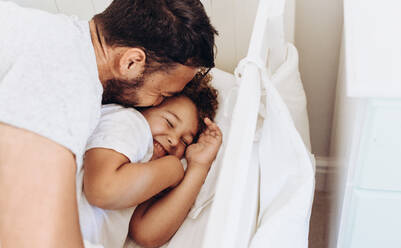 Cheerful father and son having fun at home. Man pampering and waking up his son on bed. - JLPSF16995