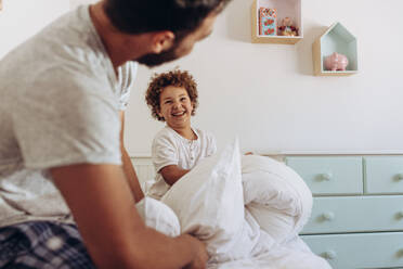 Father and son having a pillow fight sitting on bed. Cheerful man and kid playing with pillows on bed. - JLPSF17000