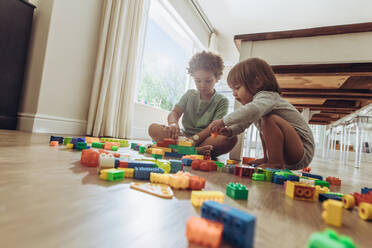 Zwei Kinder sitzen auf dem Boden und spielen mit Bauklötzen. Geschwister spielen mit Spielzeug zu Hause. - JLPSF17008