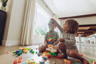 Kinder bauen einen Turm aus Bauklötzen. Glückliche Kinder spielen mit Spielzeug auf dem Boden sitzend zu Hause. - JLPSF17010