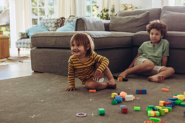 Zwei Kinder sitzen mit ihren Spielsachen auf dem Boden und spielen. Kinder spielen zu Hause mit Bauklötzen. - JLPSF17026