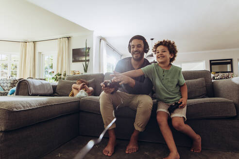 Fröhlicher Vater und Sohn genießen Videospiel zu Hause. Mann spielt Videospiel sitzt auf Couch zu Hause mit seinem Sohn. - JLPSF17032