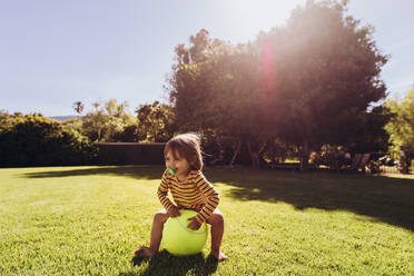 Kleiner Junge spielt mit Ball in einem Park an einem sonnigen Tag. Lächelnder Junge spielt allein im Park mit Sonne Flare im Hintergrund. - JLPSF17034