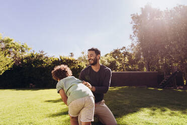 Vater und Sohn spielen an einem sonnigen Tag im Park. Ein lächelnder Mann verbringt Zeit mit seinem Sohn im Freien - JLPSF17036