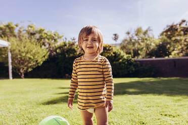 Porträt eines Jungen, der allein im Park steht und weint. Kleiner Junge, der an einem sonnigen Tag in einem Park mit einem Ball spielt. - JLPSF17040