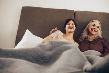 Happy daughter and mother lying on bed at home and laughing together. Smiling woman spending happy time with her mother lying on bed. - JLPSF17051