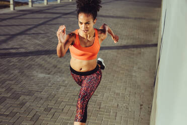 Fit young woman sprinting on the pavement. Female in sportswear running fast at the promenade. - JLPSF17101