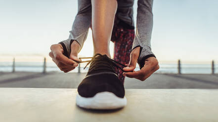 Woman tying her laces before a run. Female runner tying her shoelaces while training outdoor on a road by the sea. - JLPSF17103