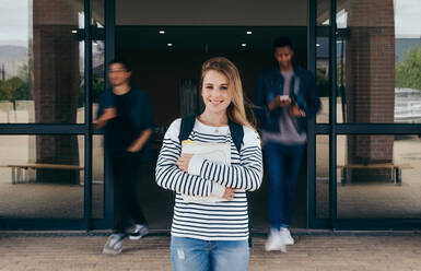 Confident female student standing at university campus with other students walking in background. Young woman standing in college with students walking at the back in motion blur. - JLPSF17120