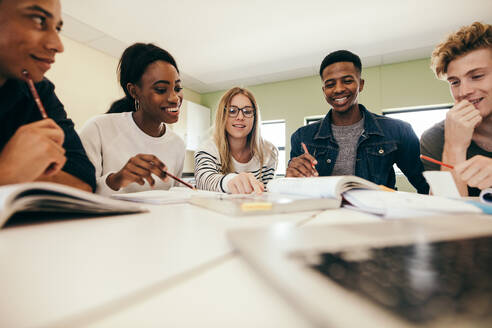 Glückliche junge Universitätsstudenten, die mit Büchern im College studieren. Gruppe von multiethnischen Menschen im Klassenzimmer. - JLPSF17126