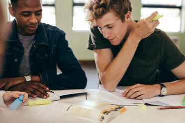 Zwei junge Studenten, die in der Bibliothek lernen und mit Büchern am Tisch sitzen. - JLPSF17137