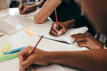 Ausschnitt von Studenten, die an einem Tisch in einem College sitzen und Notizen machen; Fokus auf die Hände von Jungen und Mädchen, die in ihre Bücher schreiben. - JLPSF17142