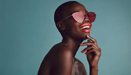 Nahaufnahme einer schönen Frau mit Sonnenbrille und roten Lippen vor grauem Hintergrund. Afrikanisches weibliches Model mit flippiger Sonnenbrille. - JLPSF17173