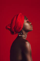Seitenansicht einer Frau mit rotem Turban im Atelier. Stilvolles weibliches Modell mit geschlossenen Augen vor rotem Hintergrund. - JLPSF17207