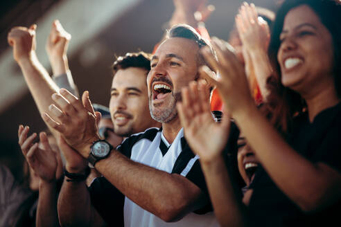 Group of men and women cheering their national team. Football team supporters enjoying during watching a live match from stadium. - JLPSF17277