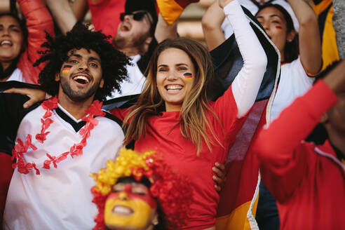 Begeisterte Sportfans bei einem Live-Spiel, die ihre Mannschaft anfeuern. Deutsche Fußballfans, die ein Fußballspiel verfolgen und ihre Nationalmannschaft anfeuern. - JLPSF17294