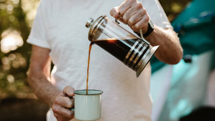 Close-up of a senior man pouring coffee in a mug at campsite. Male traveller having coffee at camping site. - JLPSF17326