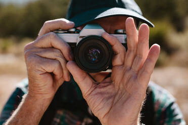 Closeup of a senior man photographing with a digital camera. Retired man taking some snaps while on hiking trip. - JLPSF17336