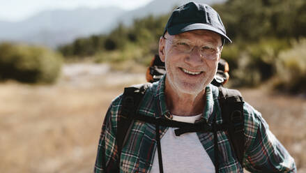Porträt eines älteren Mannes, der einen Rucksack trägt, in die Kamera schaut und lächelt. Fitter alter Mann auf einem Wanderausflug. - JLPSF17339