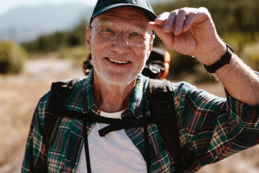 Happy senior man on hiking trip looking at camera and smiling. Fit elderly man enjoying on a hiking trip. - JLPSF17340