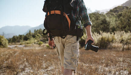 Rückansicht eines älteren Mannes mit Rucksack, der in der Natur wandert und eine Digitalkamera hält. Mann auf Wandertour. - JLPSF17342